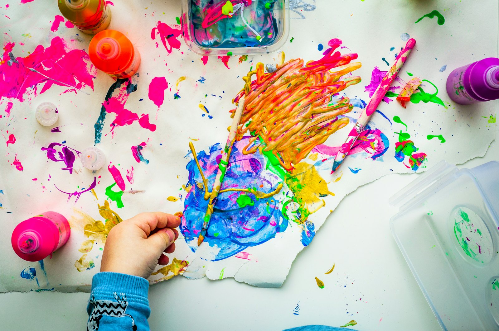 A child's paint-covered hand making a bright, colourful painting on paper